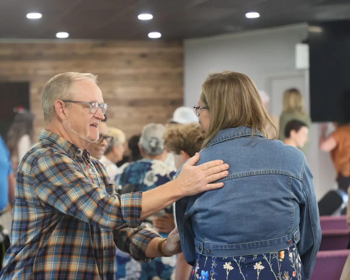 A church member greeting a woman with a hand on her shoulder after Sunday worship
